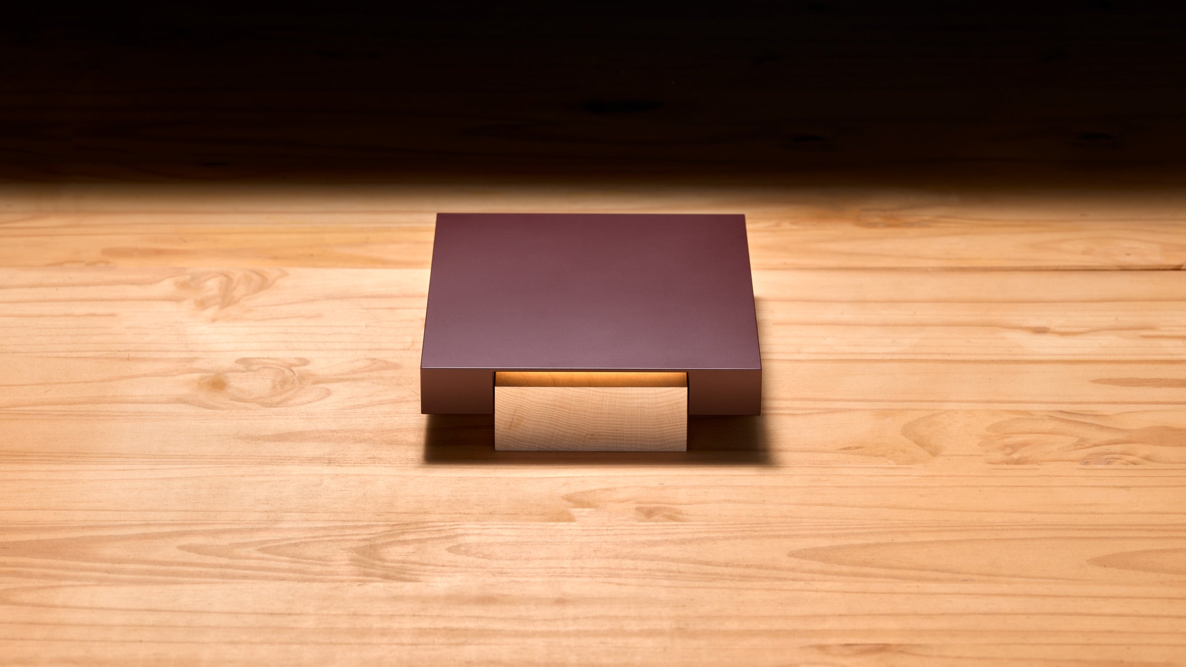 Vora Aegis on a pale wood floor under warm light, with a burgundy aluminum body resting on a solid wood block